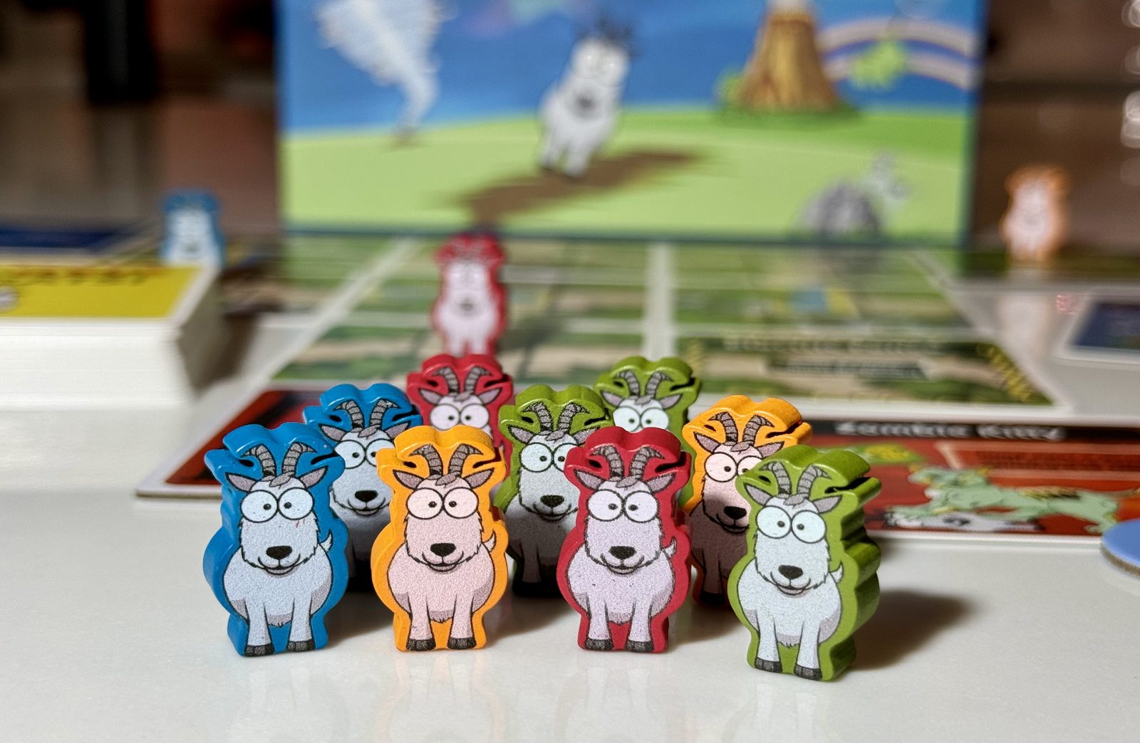A herd of colorful wooden goat-shaped tokens standing in front of the We Have Goats game board